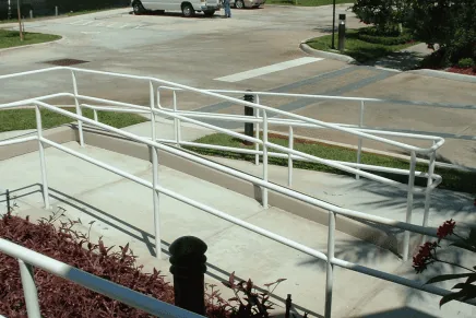 Accessible ramp and concrete walkway route with handrails near a parking area