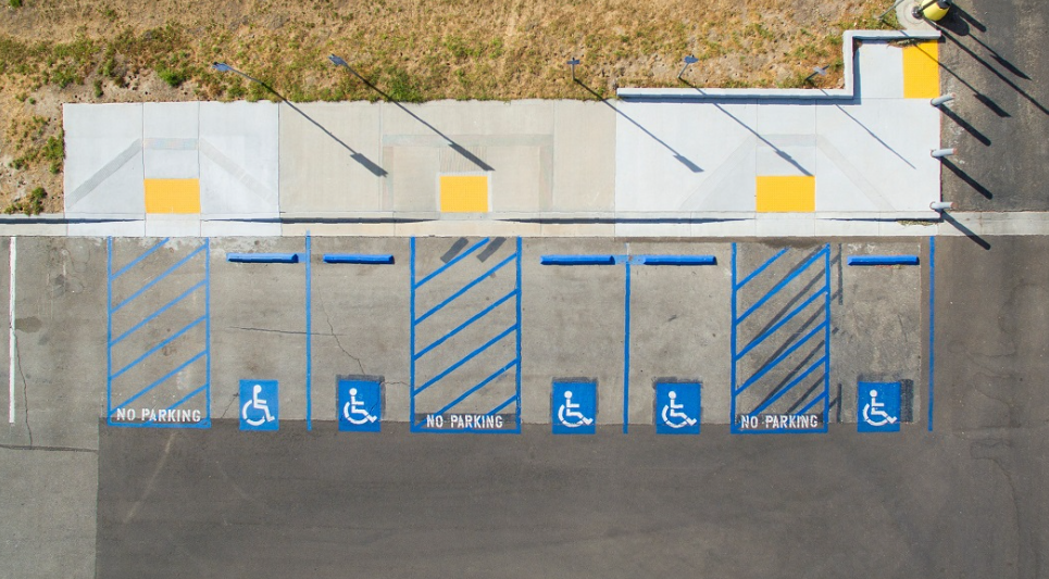 Aerial view of accessible parking stalls, striped access aisles, wheel stops, curb ramps, and a sidewalk route