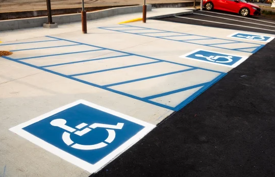 Concrete accessible parking stalls and access aisles adjacent to an asphalt parking lot
