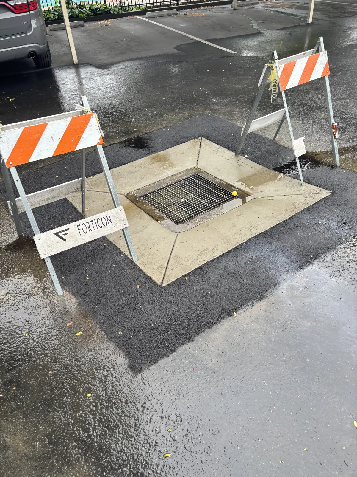 Completed concrete drain skirt surrounding a drainage inlet within an asphalt parking lot