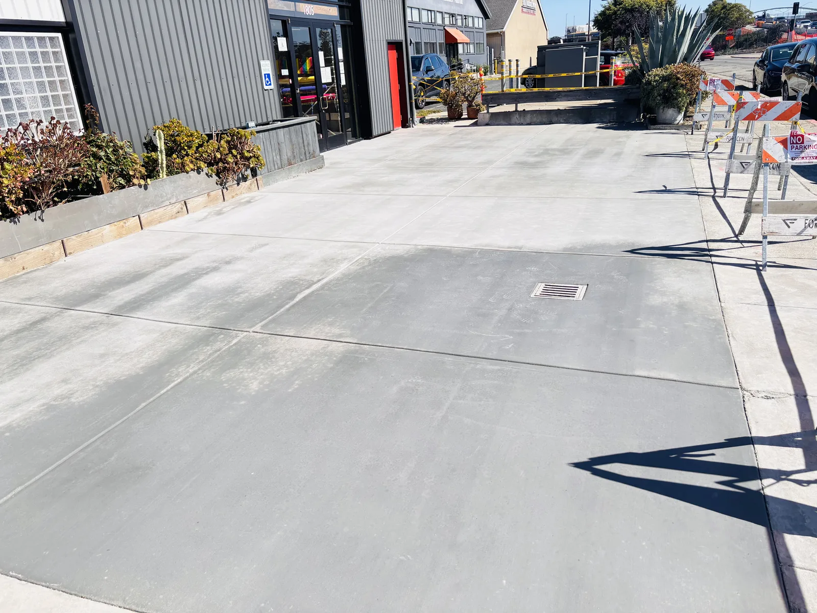 Finished commercial concrete flatwork at a building entrance with a drainage inlet and pedestrian access