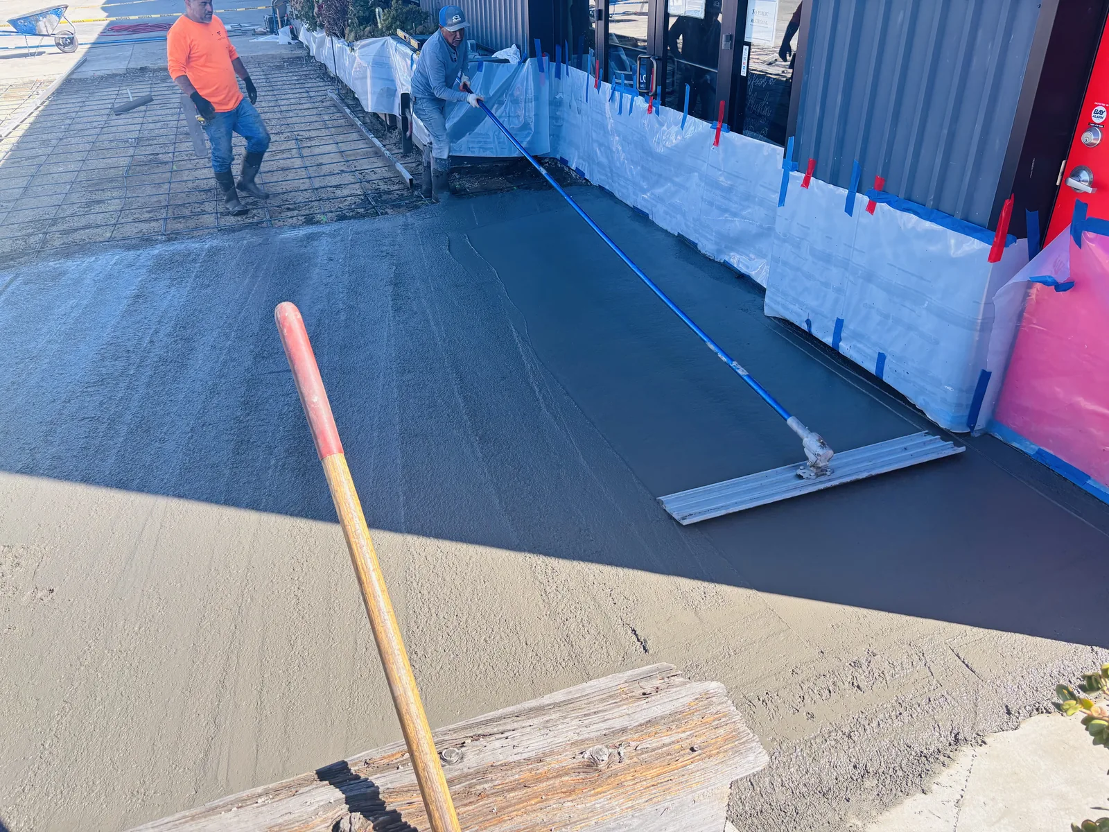 Crew screeding fresh concrete along a commercial building entrance during flatwork placement
