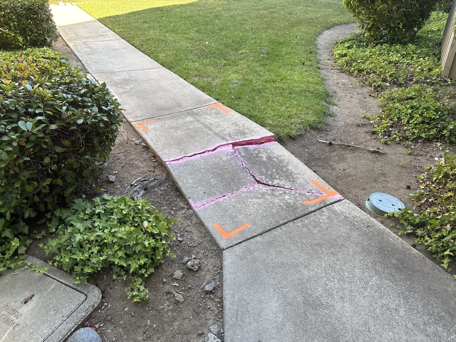 Marked cracked and lifted sidewalk panels creating a trip hazard on a pedestrian route