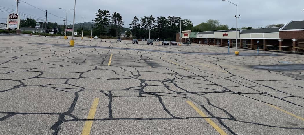 Wide commercial parking lot with many cracks filled across the pavement